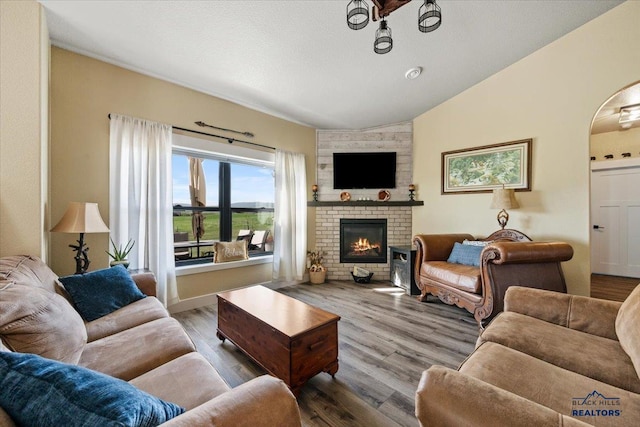 8009 Brooks Loop, Spearfish, SD 57783 - living room with vaulted ceiling, a brick fireplace, wood finished floors, and arched walkways