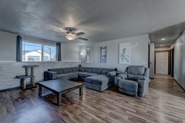 22970 Candlelight Dr, Rapid City, SD 57703 - living room featuring a textured ceiling, a ceiling fan, wood finished floors, a wood stove, and a wainscoted wall