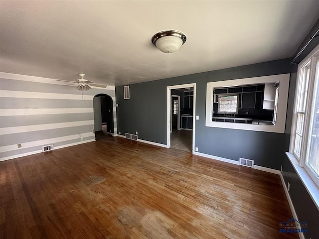 204 3rd Ave, Edgemont, SD 57735 - unfurnished living room with arched walkways, wood finished floors, ceiling fan, baseboards, and healthy amount of natural light