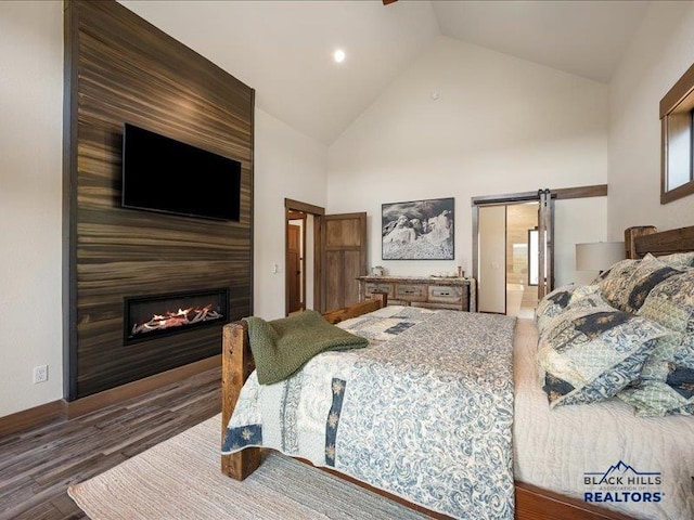 11311 Overlook Ct, Lead, SD 57754 - bedroom with wood finished floors, high vaulted ceiling, a fireplace, and a barn door