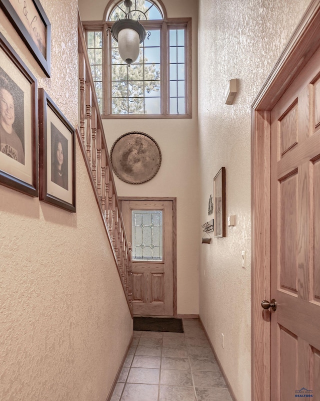 7410 Pinewood Ct, Rapid City, SD 57702 - doorway to outside featuring a textured wall, stairs, a high ceiling, light tile patterned floors, and baseboards