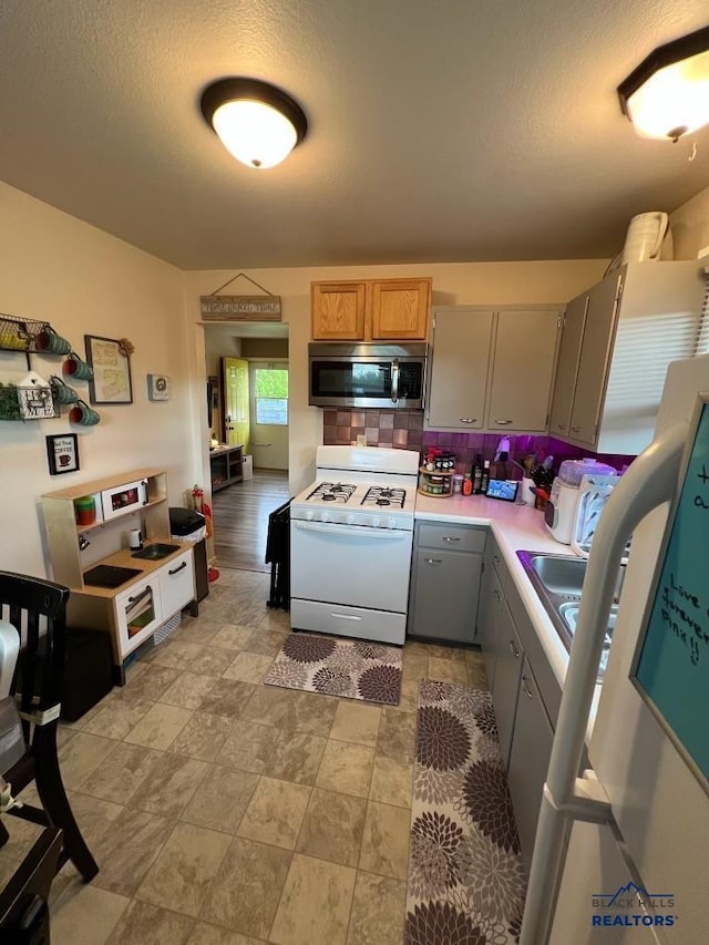 2104 Colorado, Sturgis, SD 57785 - kitchen with stainless steel microwave, white range with gas stovetop, decorative backsplash, light countertops, and gray cabinetry