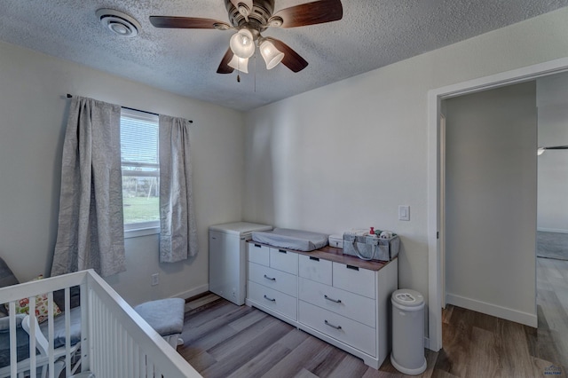 426 E Oakland, Rapid City, SD 57701 - bedroom featuring a textured ceiling, light wood-type flooring, baseboards, a crib, and a ceiling fan
