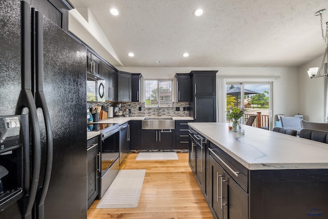 2909 Hoefer Ave, Rapid City, SD 57701 - kitchen featuring stainless steel appliances, light wood-style floors, a textured ceiling, a center island, and backsplash