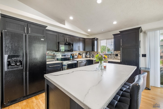 2909 Hoefer Ave, Rapid City, SD 57701 - kitchen featuring black appliances, vaulted ceiling, backsplash, light wood finished floors, and a center island