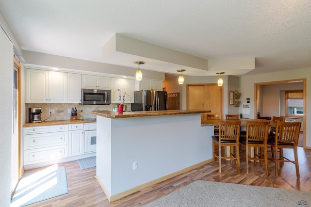 4941 Springtree Ct, Rapid City, SD 57702 - kitchen with stainless steel appliances, tasteful backsplash, white cabinetry, light wood-style flooring, and pendant lighting