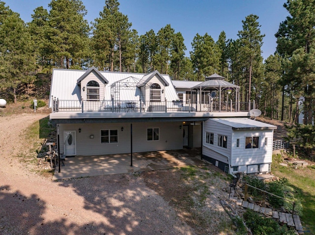 12525 Jax Ct, Rapid City, SD 57701 - back of house with a metal roof, a gazebo, a wooden deck, view of scattered trees, and a patio