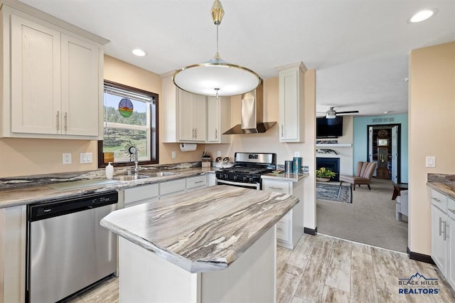 28085 Hargins Rd, Hot Springs, SD 57747 - kitchen featuring stainless steel appliances, wall chimney exhaust hood, a center island, a ceiling fan, and a fireplace