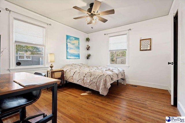 bedroom with multiple windows, wood finished floors, visible vents, and baseboards