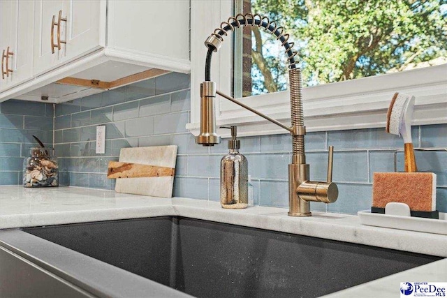 details featuring white cabinets, decorative backsplash, a sink, and light countertops