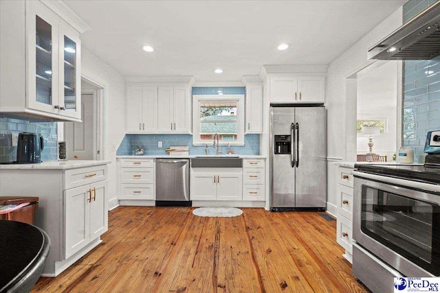 kitchen featuring white cabinets, stainless steel appliances, light countertops, wall chimney range hood, and a sink