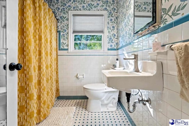 bathroom with wainscoting, toilet, and wallpapered walls