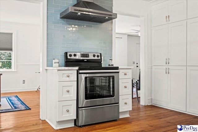 kitchen with light countertops, electric range, white cabinets, light wood-type flooring, and wall chimney exhaust hood