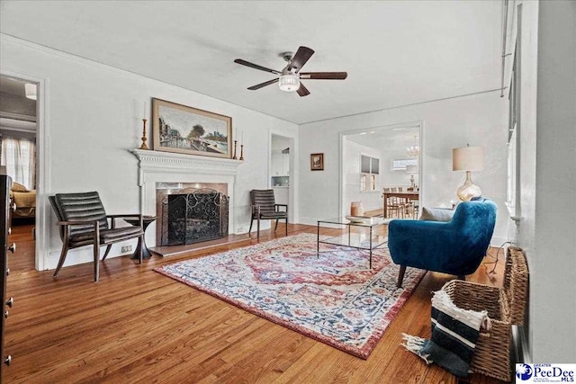 living area with ceiling fan, a fireplace with raised hearth, and wood finished floors