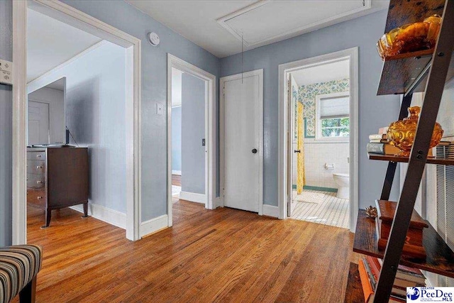 corridor featuring attic access, baseboards, and wood finished floors