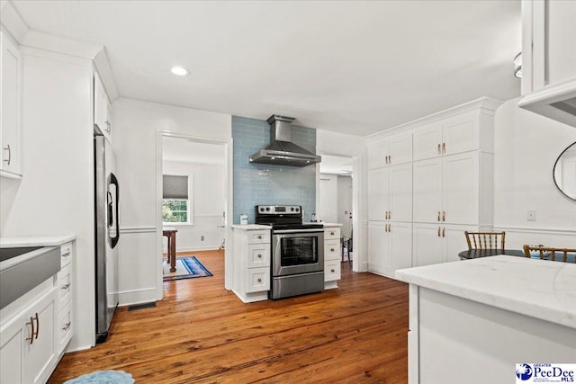 kitchen with appliances with stainless steel finishes, white cabinets, wall chimney range hood, and wood finished floors