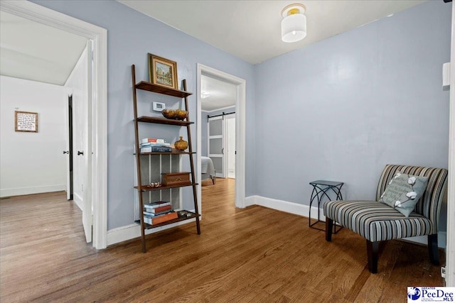 living area featuring a barn door, baseboards, and wood finished floors