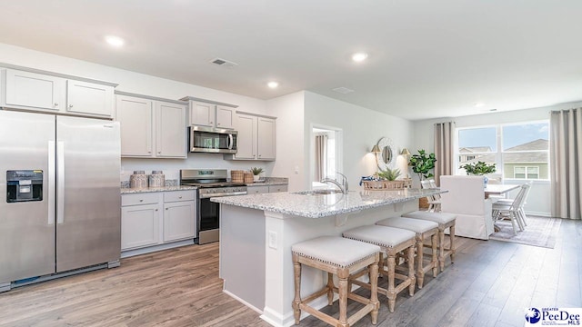 kitchen featuring a breakfast bar, sink, a kitchen island with sink, stainless steel appliances, and light stone countertops