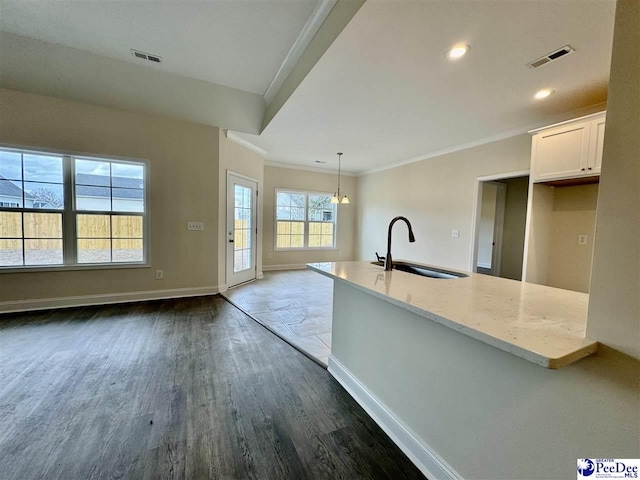 kitchen with decorative light fixtures, sink, white cabinets, light stone counters, and crown molding