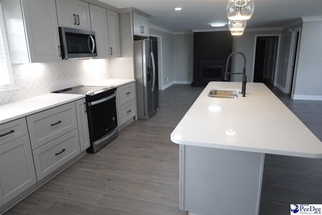 kitchen with sink, crown molding, dark hardwood / wood-style flooring, stainless steel appliances, and a kitchen island with sink