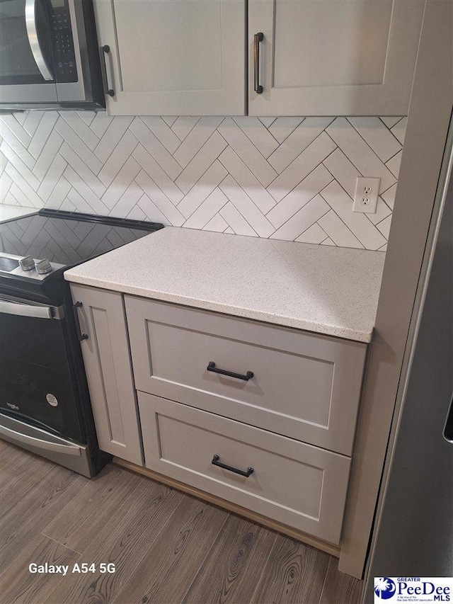 kitchen with hardwood / wood-style flooring, stainless steel appliances, gray cabinets, and decorative backsplash