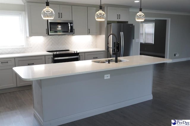 kitchen featuring appliances with stainless steel finishes, backsplash, ornamental molding, a center island with sink, and decorative light fixtures