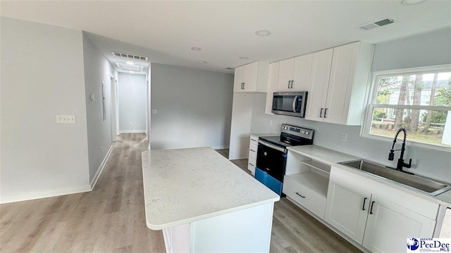 kitchen with sink, white cabinetry, light wood-type flooring, appliances with stainless steel finishes, and a kitchen island