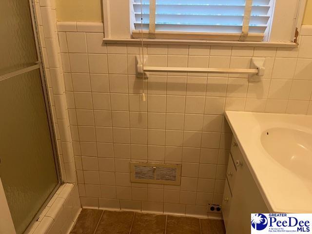 bathroom featuring an enclosed shower, vanity, tile patterned floors, and tile walls