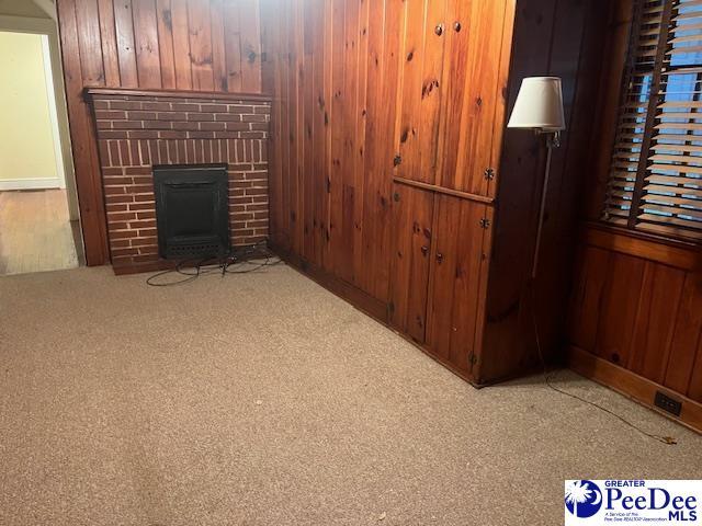 living room featuring light carpet, a fireplace, and wooden walls