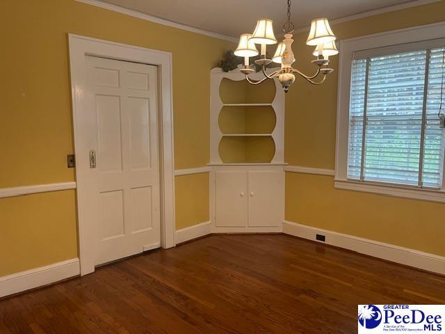 unfurnished dining area featuring crown molding, dark wood-type flooring, and a notable chandelier