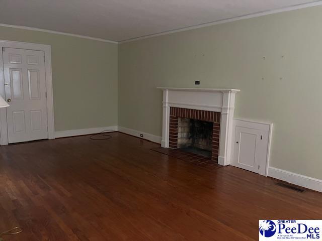 unfurnished living room with a brick fireplace, crown molding, and dark hardwood / wood-style floors