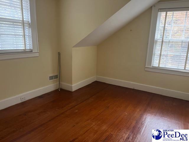 additional living space featuring lofted ceiling, dark wood-type flooring, and plenty of natural light