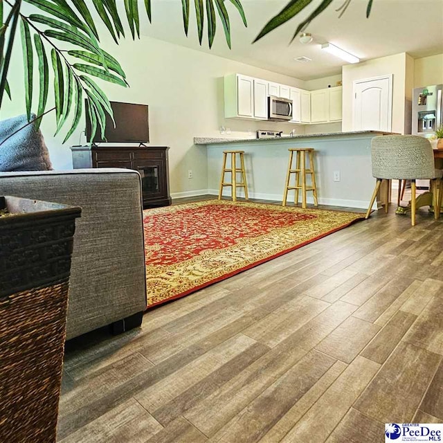 822 Twin Oaks Cir, Lake City, SC 29560 - kitchen featuring stainless steel microwave, wood finished floors, baseboards, white cabinetry, and a kitchen breakfast bar