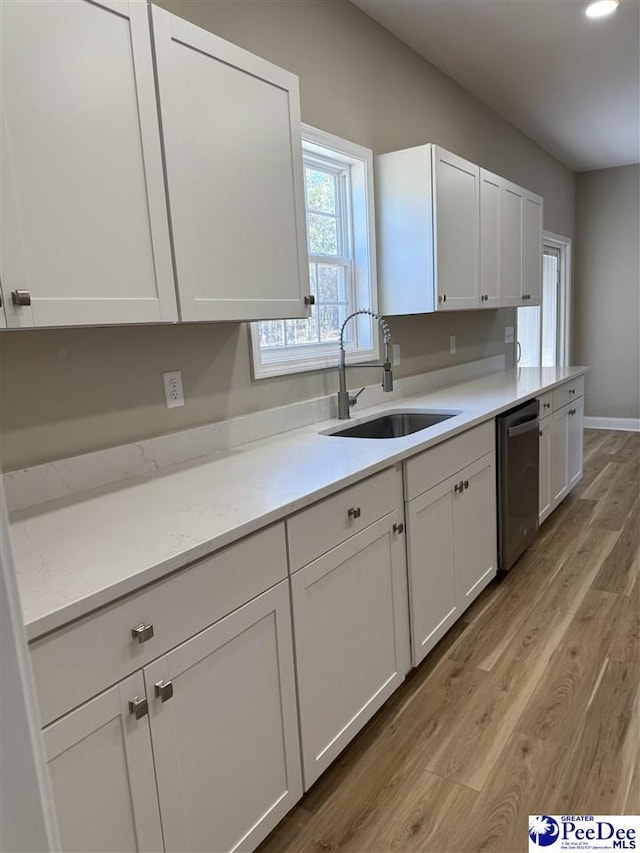 kitchen with sink, white cabinets, stainless steel dishwasher, light stone counters, and light wood-type flooring