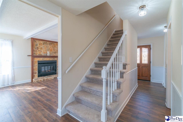 stairs with a stone fireplace, beam ceiling, wood finished floors, and a textured ceiling