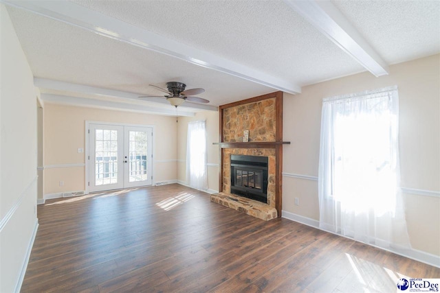 unfurnished living room with a healthy amount of sunlight, dark wood finished floors, beam ceiling, french doors, and a textured ceiling