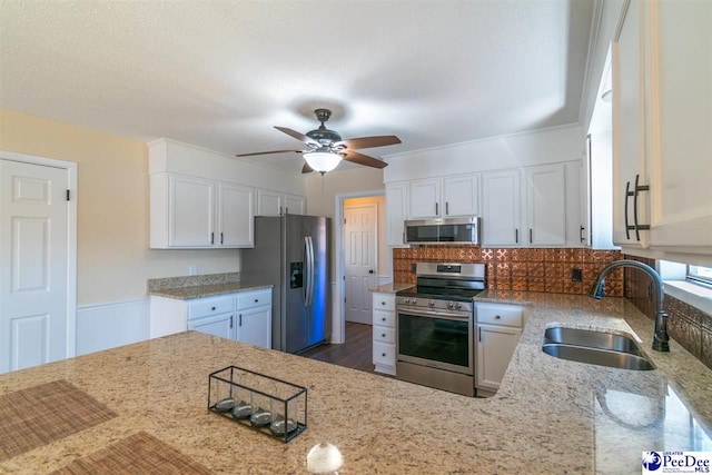 kitchen with a sink, stainless steel appliances, light stone countertops, and white cabinets