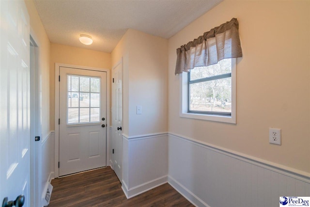 doorway to outside with a textured ceiling, a healthy amount of sunlight, dark wood finished floors, and wainscoting