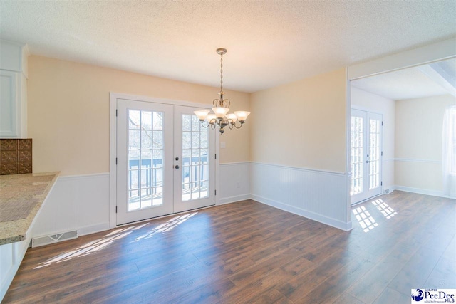 unfurnished dining area with wood finished floors, an inviting chandelier, wainscoting, visible vents, and french doors