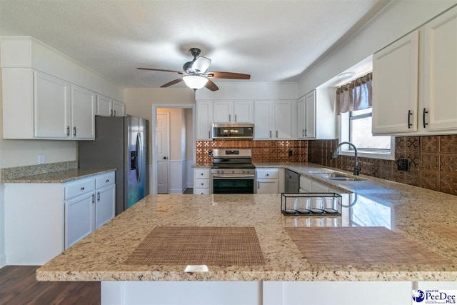 kitchen with a sink, tasteful backsplash, white cabinetry, appliances with stainless steel finishes, and light stone countertops