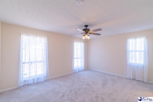 carpeted spare room with a textured ceiling, a healthy amount of sunlight, and a ceiling fan