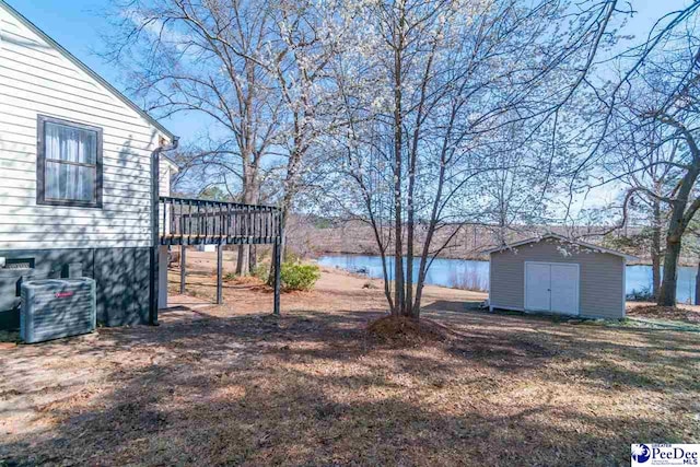 view of yard featuring a storage shed, a deck with water view, central air condition unit, and an outbuilding