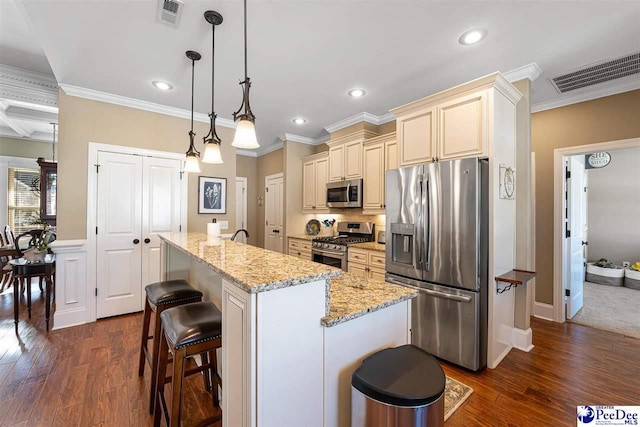 kitchen with appliances with stainless steel finishes, hanging light fixtures, light stone countertops, an island with sink, and cream cabinetry