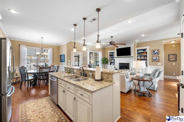 kitchen with pendant lighting, sink, stainless steel appliances, light stone countertops, and a center island with sink