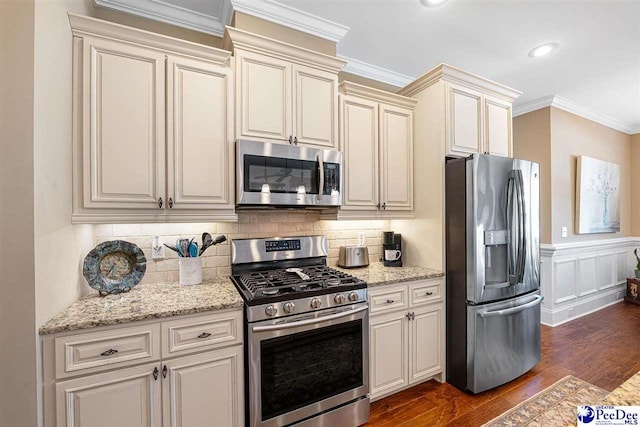 kitchen with dark hardwood / wood-style floors, ornamental molding, light stone countertops, stainless steel appliances, and cream cabinets