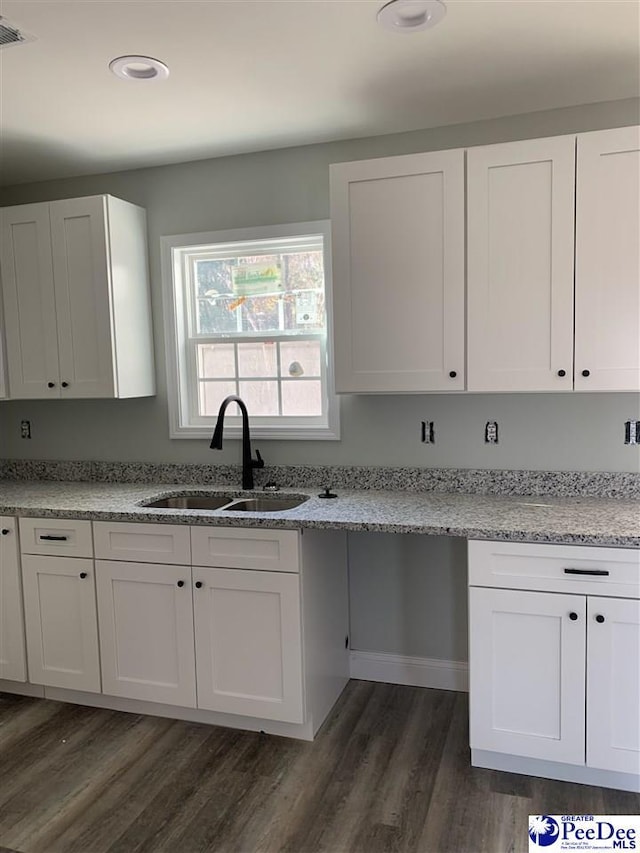 kitchen featuring light stone counters, a sink, and white cabinets