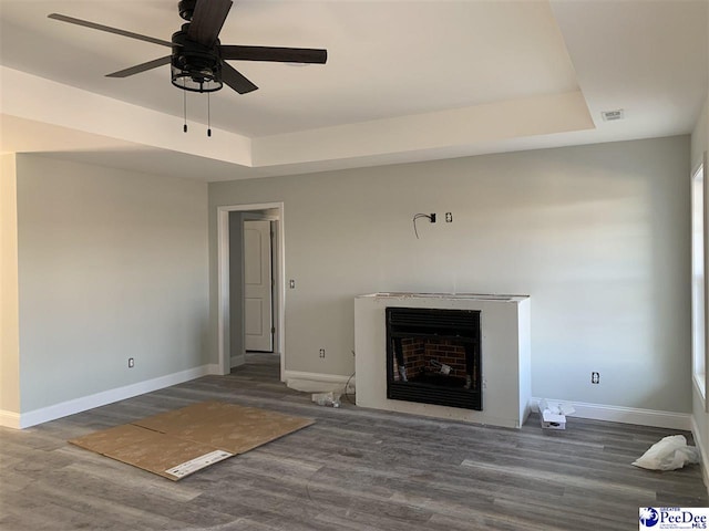 unfurnished living room with dark wood finished floors, a raised ceiling, and a fireplace