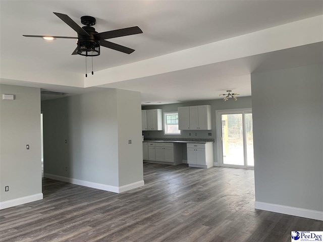 unfurnished living room with dark wood finished floors, baseboards, and ceiling fan