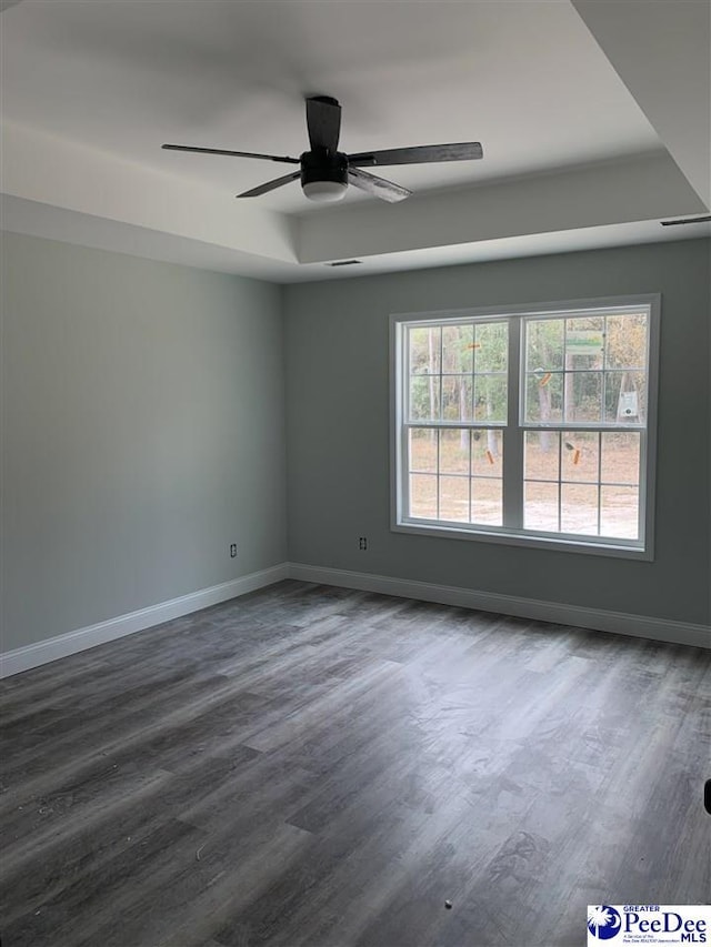 spare room featuring dark wood-style floors, baseboards, a tray ceiling, and ceiling fan