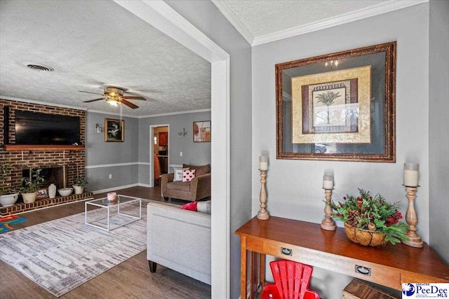 living room featuring hardwood / wood-style floors, ornamental molding, a textured ceiling, and a brick fireplace